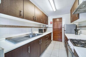 A modern kitchen with dark wooden cabinets, a stainless steel sink, a microwave, and a gas stove. - Arauco Urban - Apart in Las Condes near Parque Arauco (Las Condes)