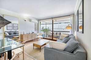 Un salon moderne avec une table à manger en verre, un canapé gris et une vue sur la ville grâce à de grandes fenêtres.