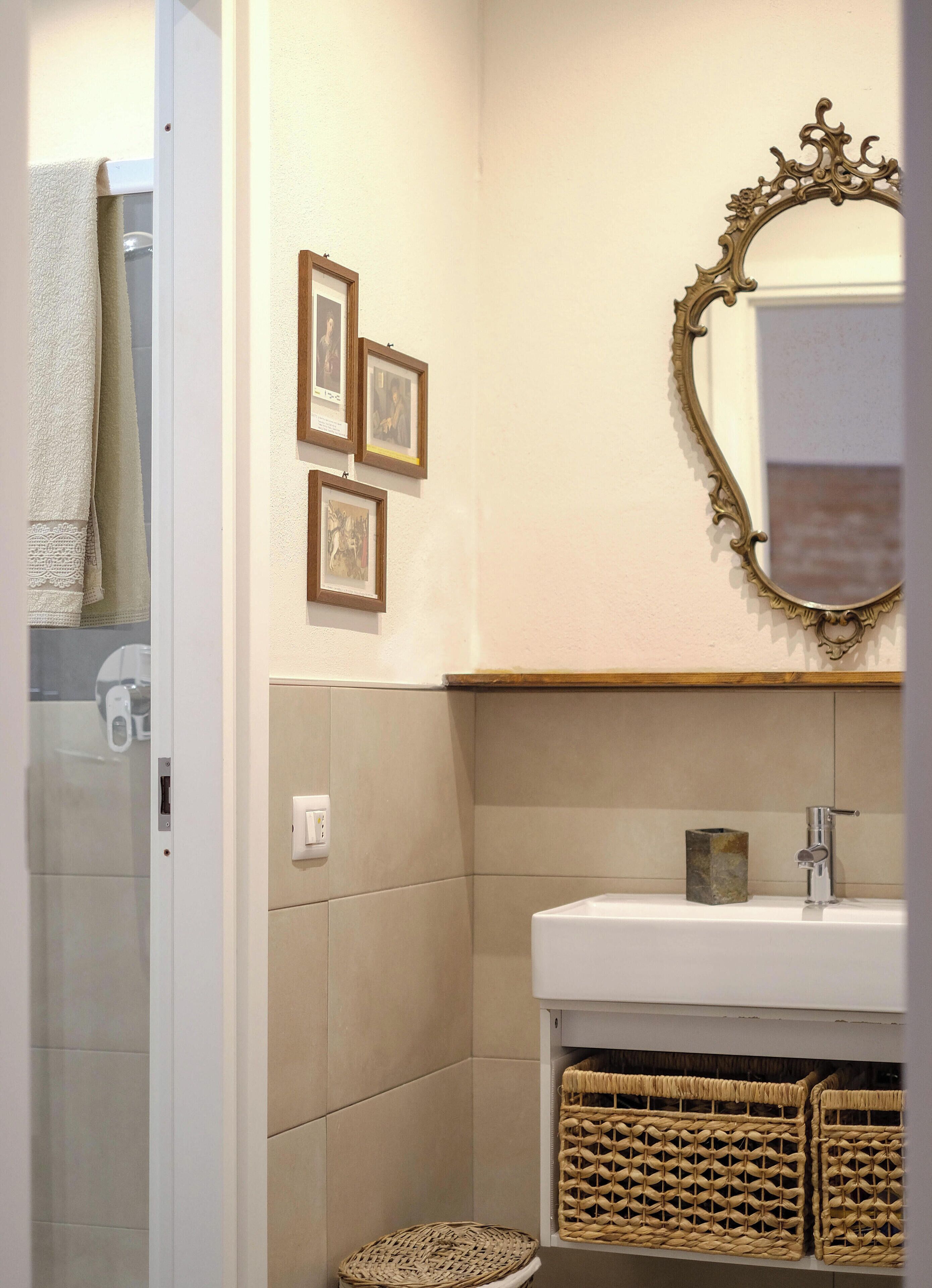 A bathroom with a white sink, a mirror with an ornate frame, and three framed pictures on the wall.