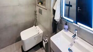 A modern bathroom with a white bathtub, a sink with a mirror, and a towel hanging on the wall. - spira.staycation (Noida)
