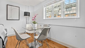 A modern dining area with a glass table and white chairs, a potted orchid, and a framed abstract artwork on the wall. - Central Soho 1-Bed - Brick Kitchen - Sleeps 4 (London)