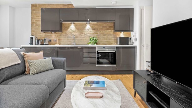 A modern kitchen with dark cabinets, a built-in oven, and a large TV. - Central Soho 1-Bed - Brick Kitchen - Sleeps 4 (London)