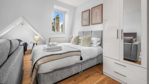 Een moderne slaapkamer met een groot bed, een kledingkast en een raam met uitzicht op gebouwen.