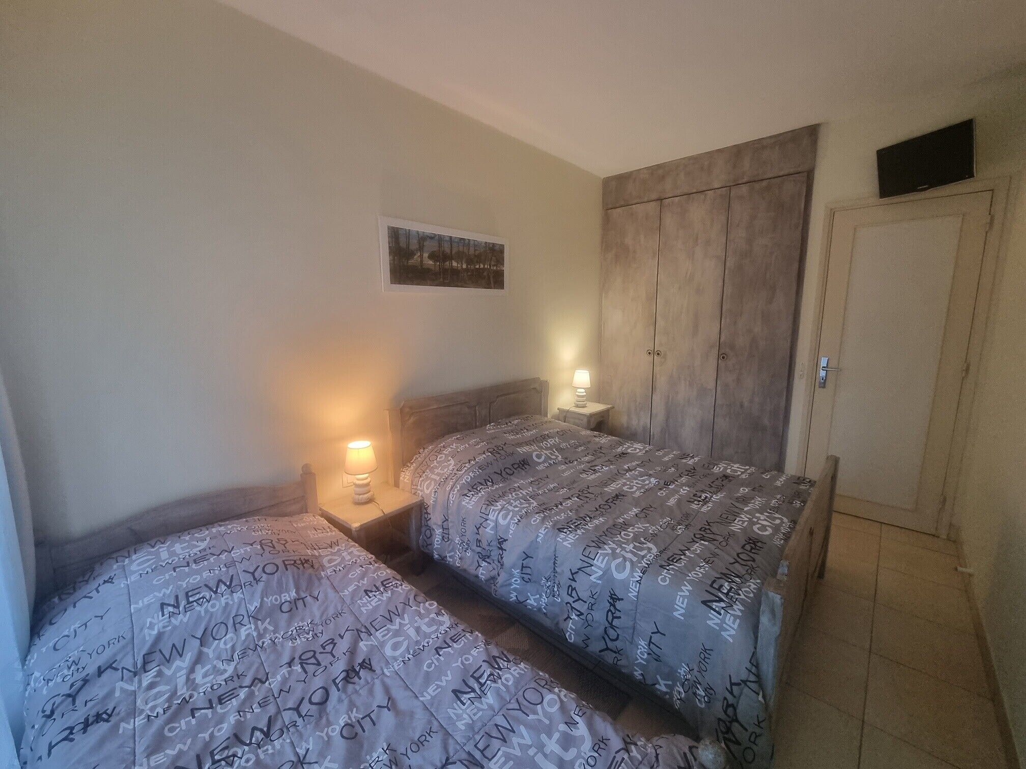A bedroom with two beds, a wardrobe, a TV, and a painting on the wall.
