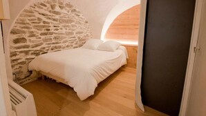 Un dormitorio con pared de piedra, techo de madera y cama con ropa de cama blanca.