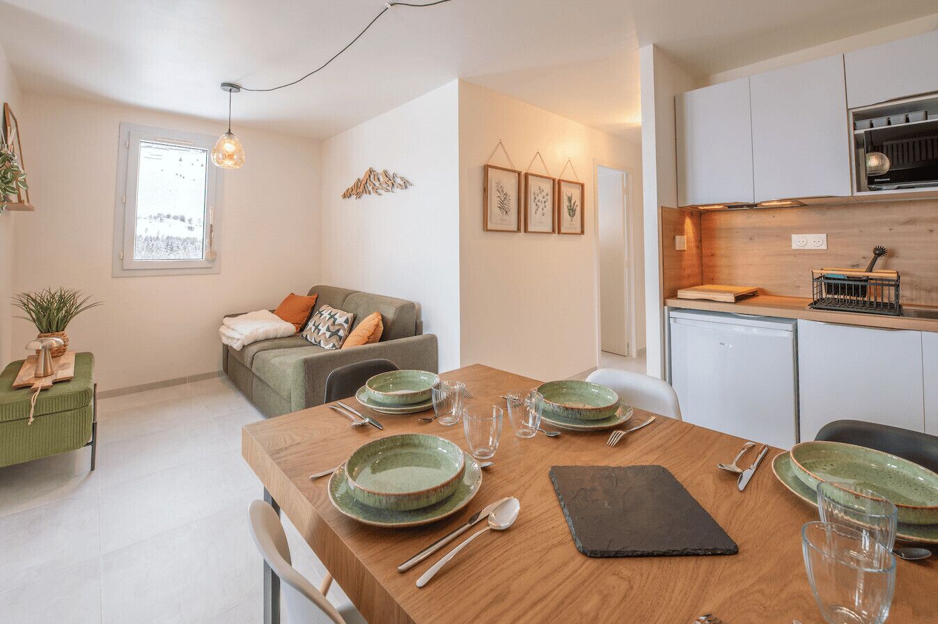 Una cucina moderna con mobili bianchi, un piano di lavoro in legno e un'area pranzo apparecchiata con piatti e posate verdi.