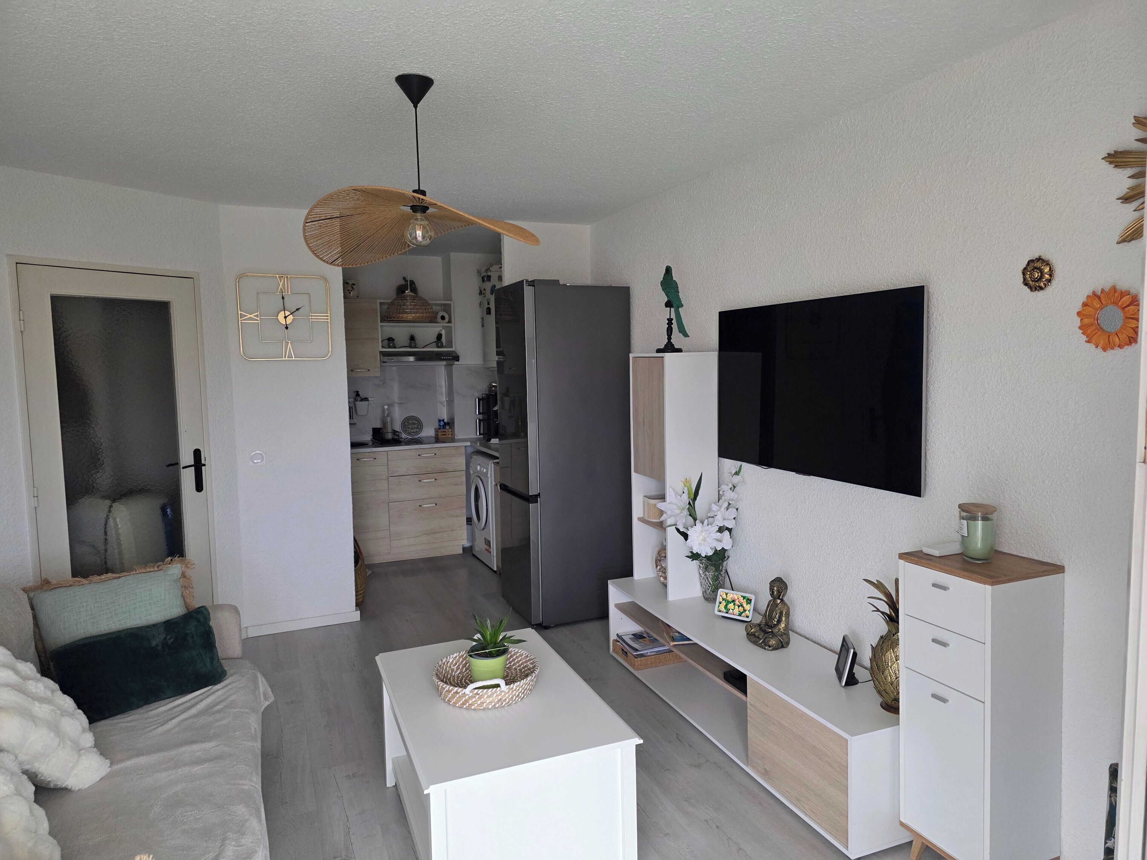 Et moderne køkken med indbygget ovn, mikroovn og køleskab. Der er et spiseområde med et hvidt bord og stole.