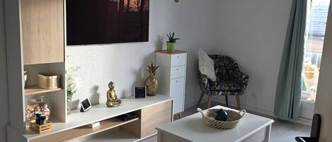 A modern living room with a flat-screen TV, a wooden cabinet, a small Buddha statue, a decorative bowl, and a chair with a floral pattern.