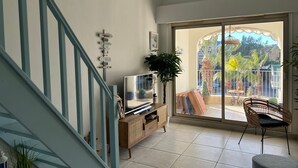 Een woonkamer met een televisie op een houten kast, een trap en een balkon met tuinmeubilair.