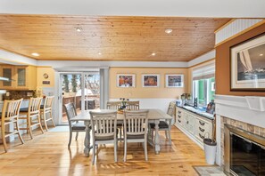 A spacious kitchen with wooden flooring, a dining area with white chairs, and a fireplace.