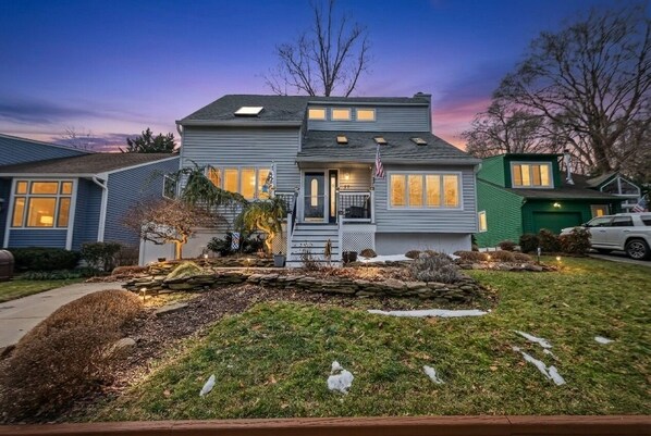 A two-story house with a front porch, a stone retaining wall, and a well-maintained lawn.