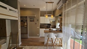 A modern kitchen with white cabinets, a wooden island with bar stools, pendant lights, and a view of the outdoors through large windows. - Bright studio apartment with terrace in Cannes (Cannes)