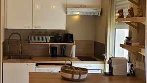 A modern kitchen with white cabinets, a stainless steel sink, and two hanging pendant lights. There is a coffee maker, a kettle, and a basket on the counter. - Bright studio apartment with terrace in Cannes (Cannes)