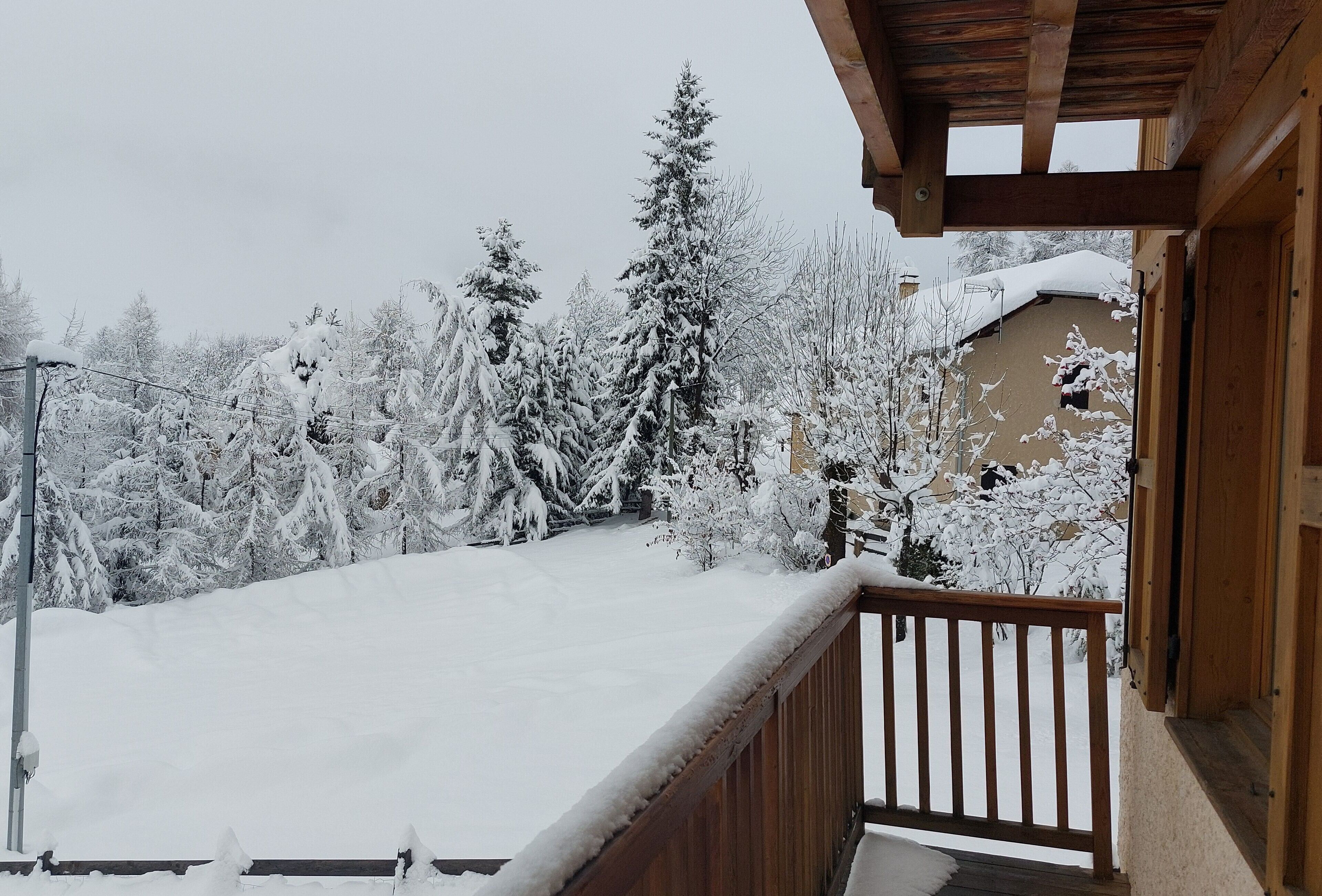 Ein Holzbalkon mit schneebedeckten Bäumen und einem Gebäude im Hintergrund.