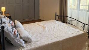 Ein Schlafzimmer mit einem Bett, einer Hängelampe, einem Fenster mit Vorhängen und einer Tür.