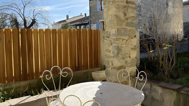 Eine überdachte Terrasse mit einem runden Tisch und Stühlen, einem Holzzaun und einer Steinmauer.