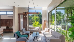 A modern living room with a large window, a sofa, a coffee table, and a TV. - Design Villa · Tulum Country Club · PGA Golf (Gran Bahía Príncipe)