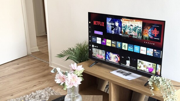 A living room with a TV displaying various streaming services, a coffee table with a magazine and remote, and a small plant.