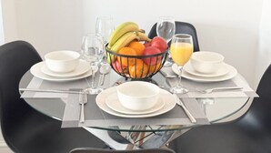A dining table set with plates, cutlery, a fruit bowl, glasses, and a glass of orange juice.