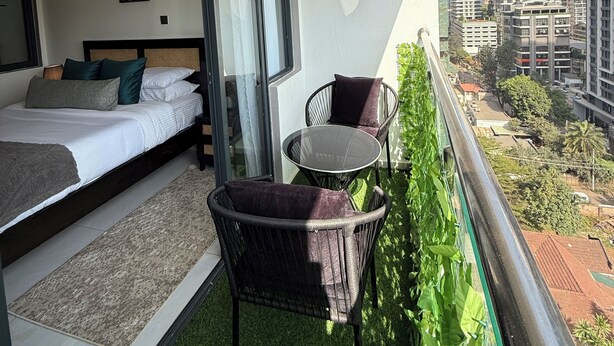 Ein Balkon mit einem Bett, einem kleinen Tisch und Stühlen mit Blick auf eine Skyline mit Hochhäusern.