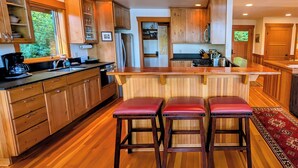 A kitchen with wooden cabinets, a large island with stools, and a view of the outdoors through a window.