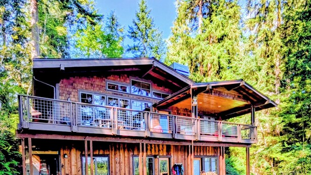 A two-story log cabin with a balcony, large windows, and a covered outdoor seating area.