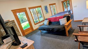A cozy room with a bed, a TV, and a fireplace. There are large windows and a view of the outdoors.