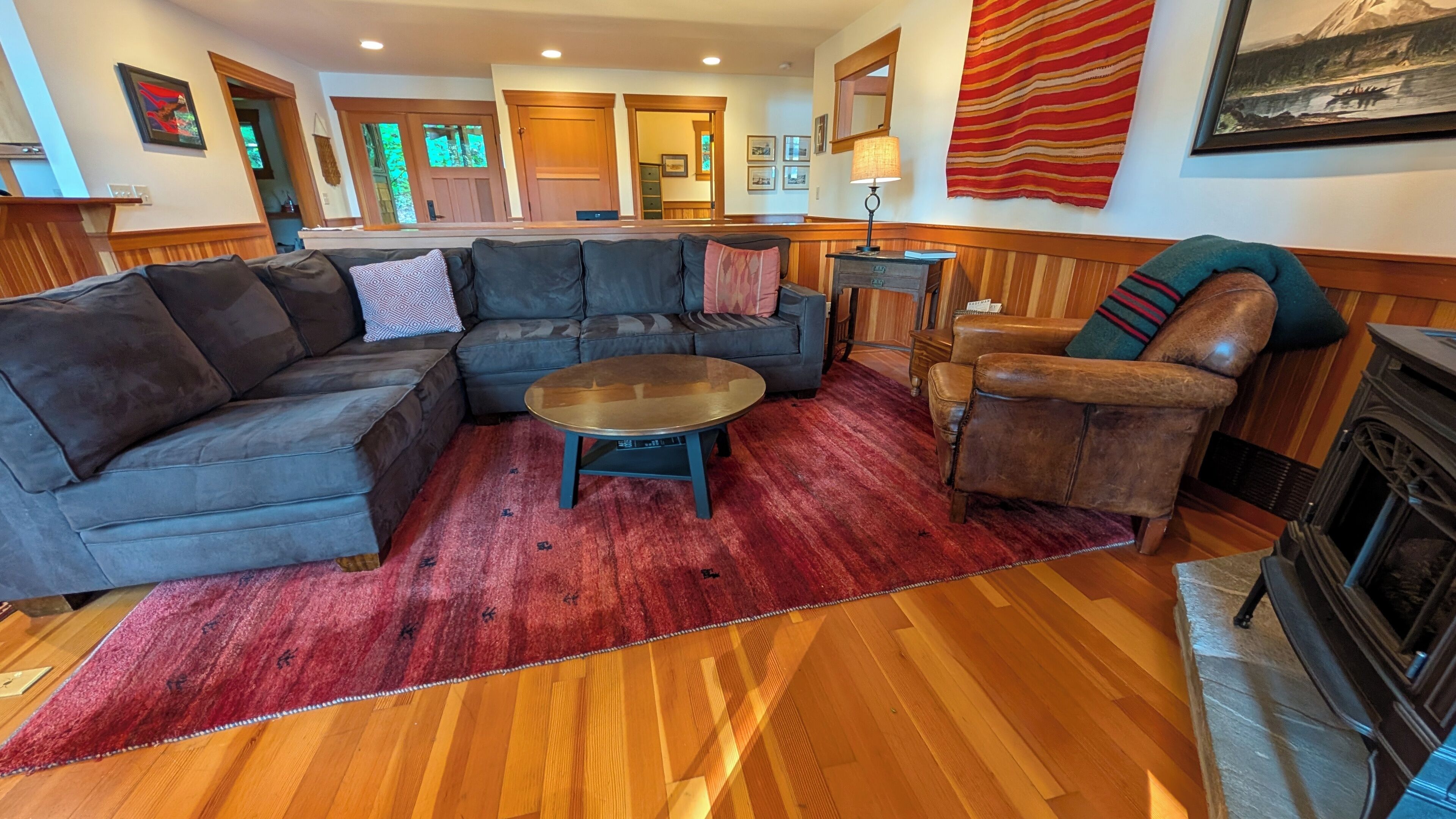 Ein Wohnzimmer mit einem Ecksofa, einem runden Couchtisch, einem Ledersessel, einem Kamin und einem roten Teppich.