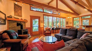 A spacious living room with a fireplace, wooden beams, large windows, and a cozy seating area.