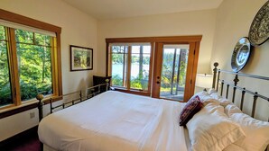 A bedroom with a large bed, a view of trees through the window, and a door leading outside.