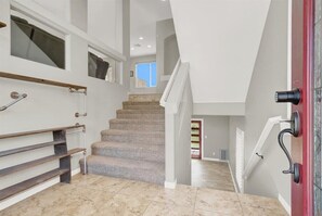 Eine Treppe mit Geländer, mit Teppich belegten Stufen und einer roten Tür mit schwarzem Griff.