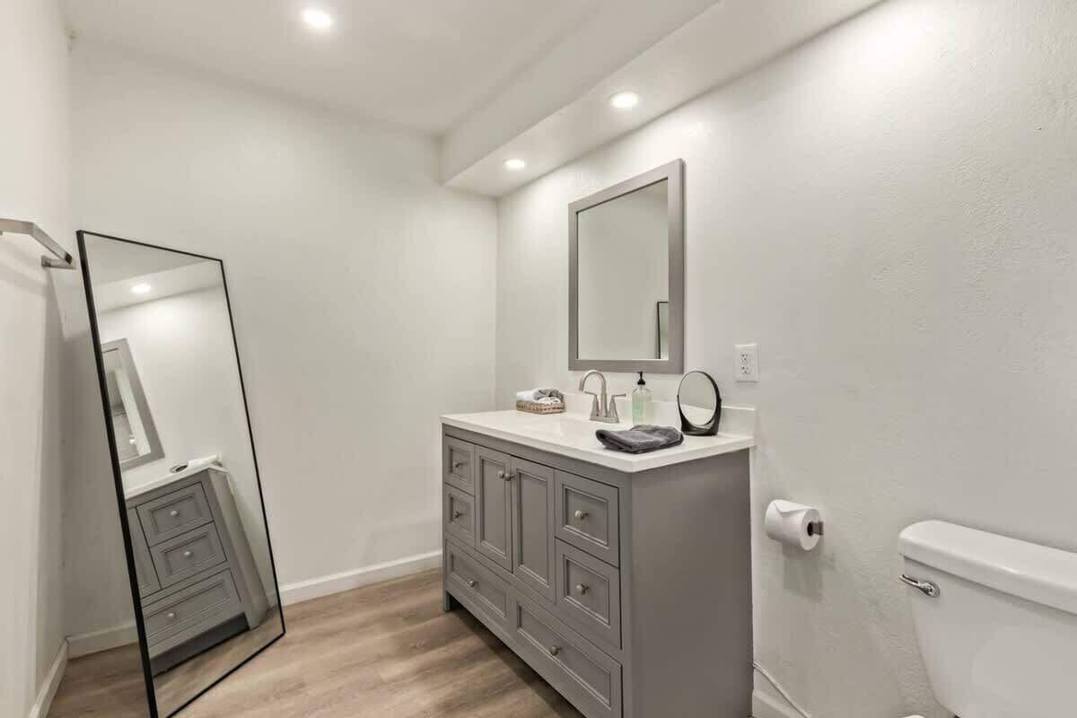 A bathroom with a grey vanity, a large mirror, a toilet, and a white sink.