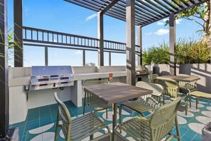 Une terrasse extérieure équipée d’un barbecue, d’un espace salon et offrant une vue sur les gratte-ciel de la ville.