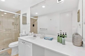 A modern bathroom with a white sink, mirror, and toilet. There are toiletries on the counter and a decorative vase. - Beachfront condo w/pool, gym & direct beach access (Hollywood)