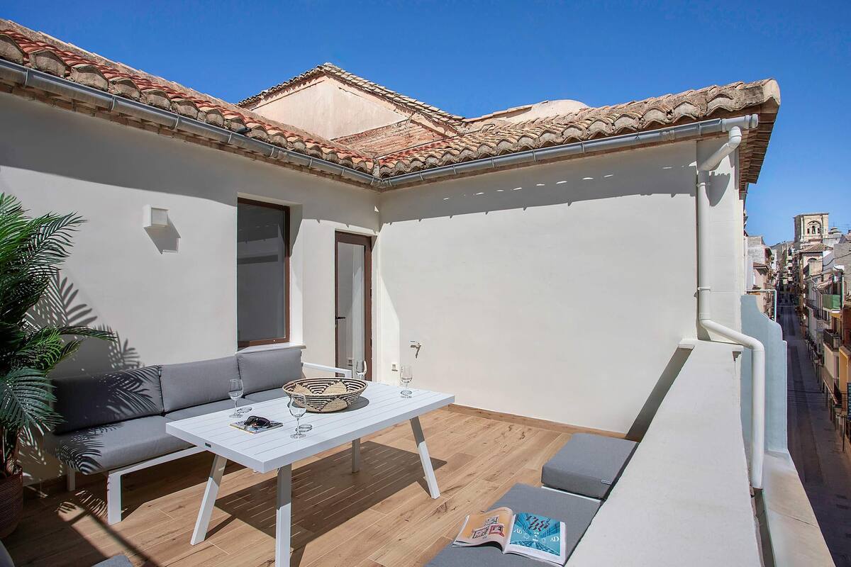 Un balcón con una mesa blanca, un sofá gris y una planta en maceta.