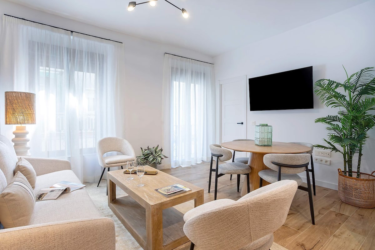 Una sala de estar moderna con sofá, mesa de centro, sillas, televisor y mesa de comedor.