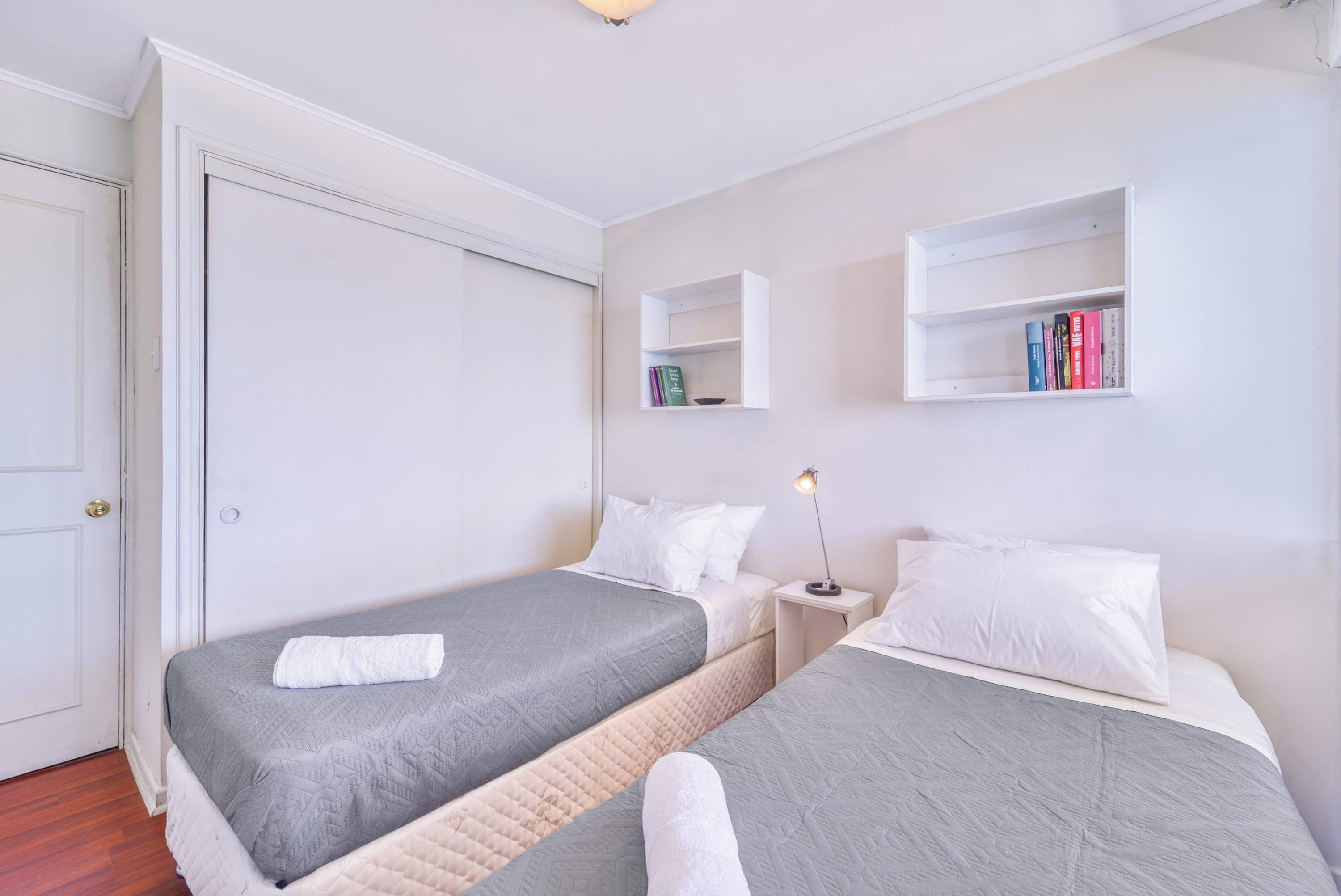 Un dormitorio con dos camas, una mesita de noche con lámpara y una estantería.