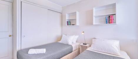 Un dormitorio con dos camas, una mesita de noche con lámpara y una estantería.