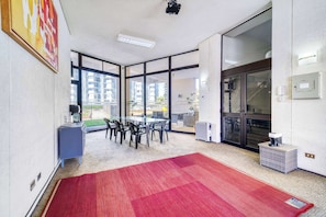 Una habitación moderna con ventanas amplias, alfombra roja, una mesa con sillas y un mueble azul.