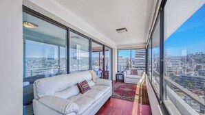 Un balcon avec un canapé blanc et une petite table, de grandes fenêtres offrant une vue sur la ville.