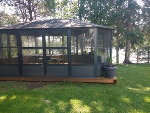 Un patio cubierto con piso de madera, paredes de vidrio y una mesa con sillas.