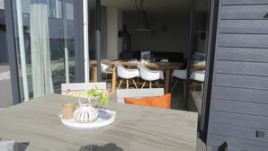 Un comedor moderno con una mesa de madera, sillas blancas y un ventanal que da a un balcón.