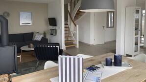 Una sala de estar moderna con un sofá, una mesa de comedor, un televisor y una escalera que sube a otro nivel.