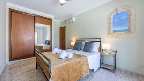 Ein Schlafzimmer mit Bett, Nachttisch, Deckenventilator, Fenster mit Blick und einem Holzschrank.
