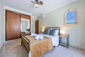 Une chambre à coucher comprenant un lit, une table de chevet, un ventilateur de plafond, une fenêtre avec vue et une armoire en bois.