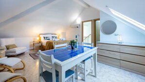 Ein modernes, helles Zimmer mit Esstisch, Stühlen, einem Bett und einem großen Fenster.