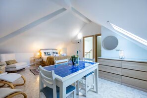 Une pièce moderne et bien éclairée, comprenant une table à manger, des chaises, un lit et une grande fenêtre.