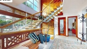 A modern interior with a wooden staircase, a bench, and a patterned rug. - Luxury Villa Aroeira (Setúbal)