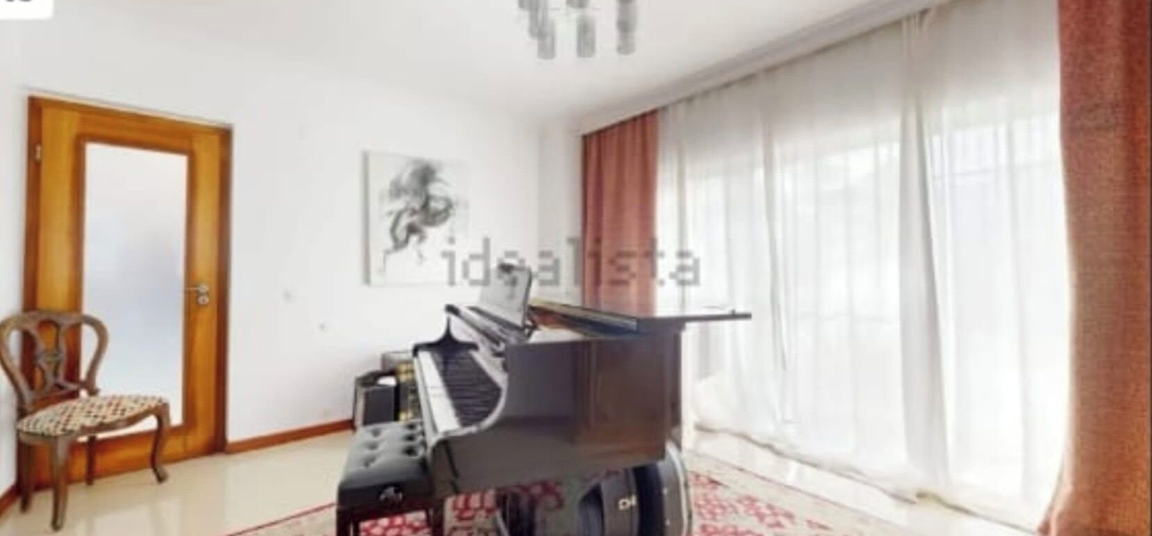 Un salón con un piano, una silla y un gran ventanal con cortinas.