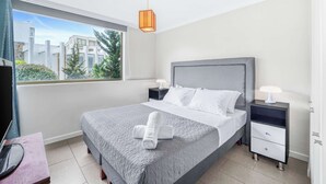 A modern hotel room with a large bed, two bedside tables, a window with a view of buildings and trees, and a ceiling light. - Central Reñaca W / Garden First Floor near Reñaca (Viña del Mar)